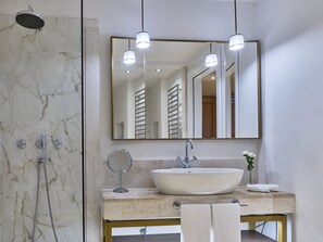 Ein modernes Badezimmer mit einer Marmerdusche, einem großen Spiegel, Pendelleuchten und einem Waschbecken mit Handtuch.