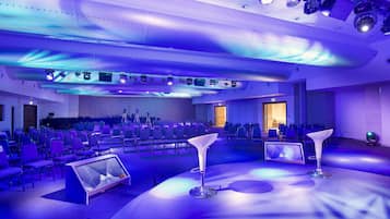 A conference room with rows of chairs, a stage with a podium, and ceiling-mounted lighting.