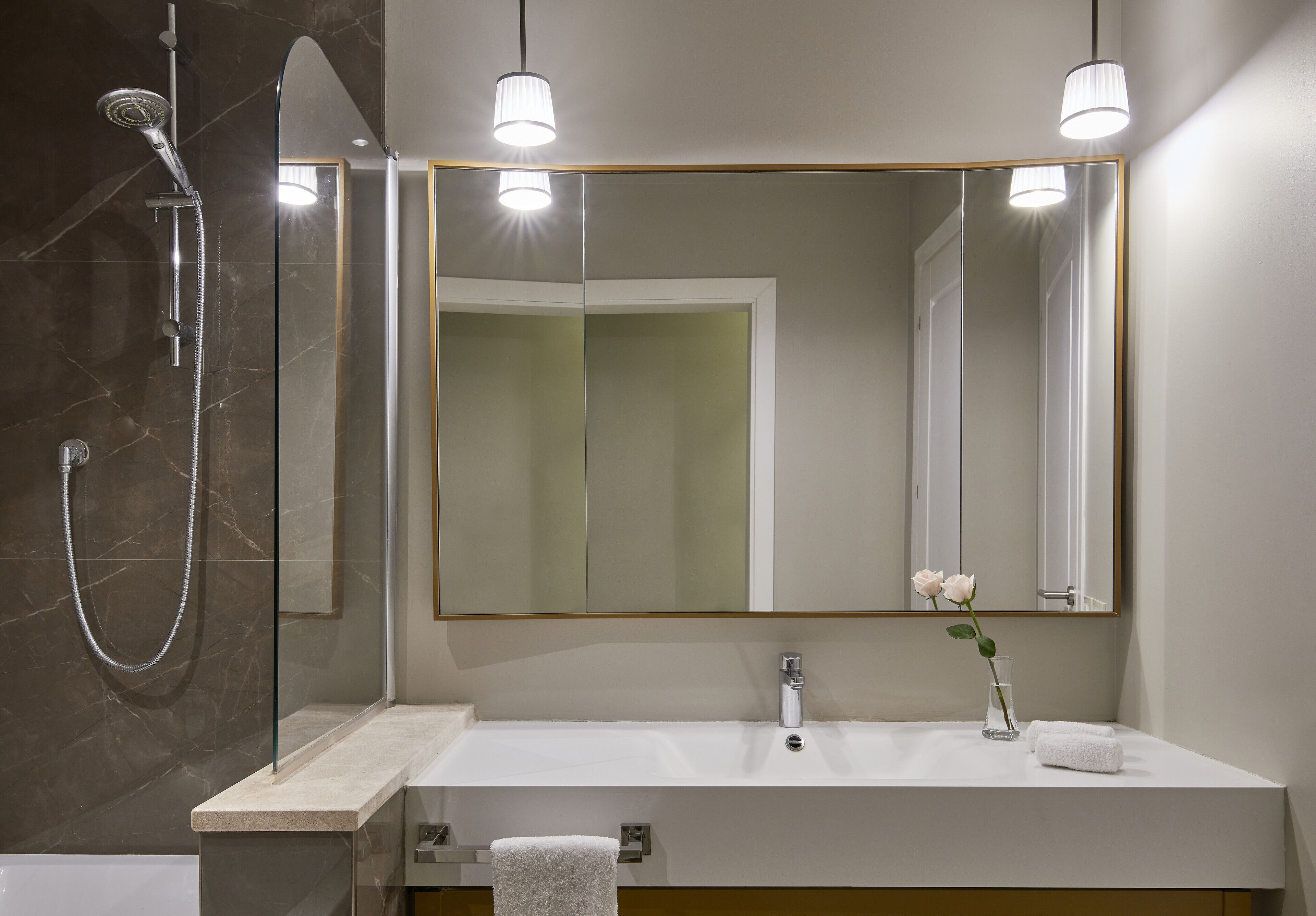 Une salle de bain moderne avec une douche à parois de verre, un lavabo blanc et un grand miroir avec un cadre doré.
