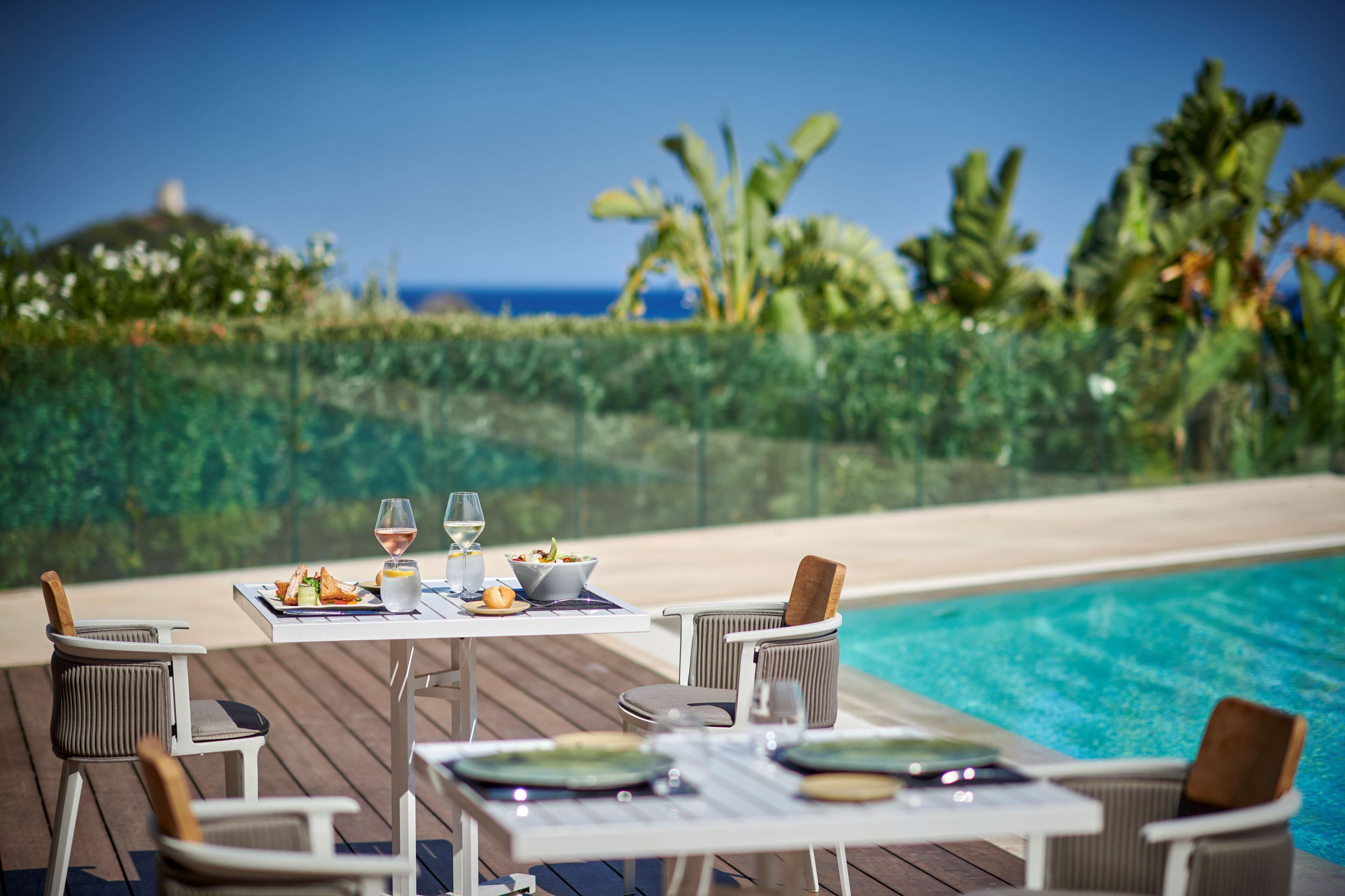 An outdoor dining area with a pool view, featuring a table set with plates, glasses, and a bowl of food.