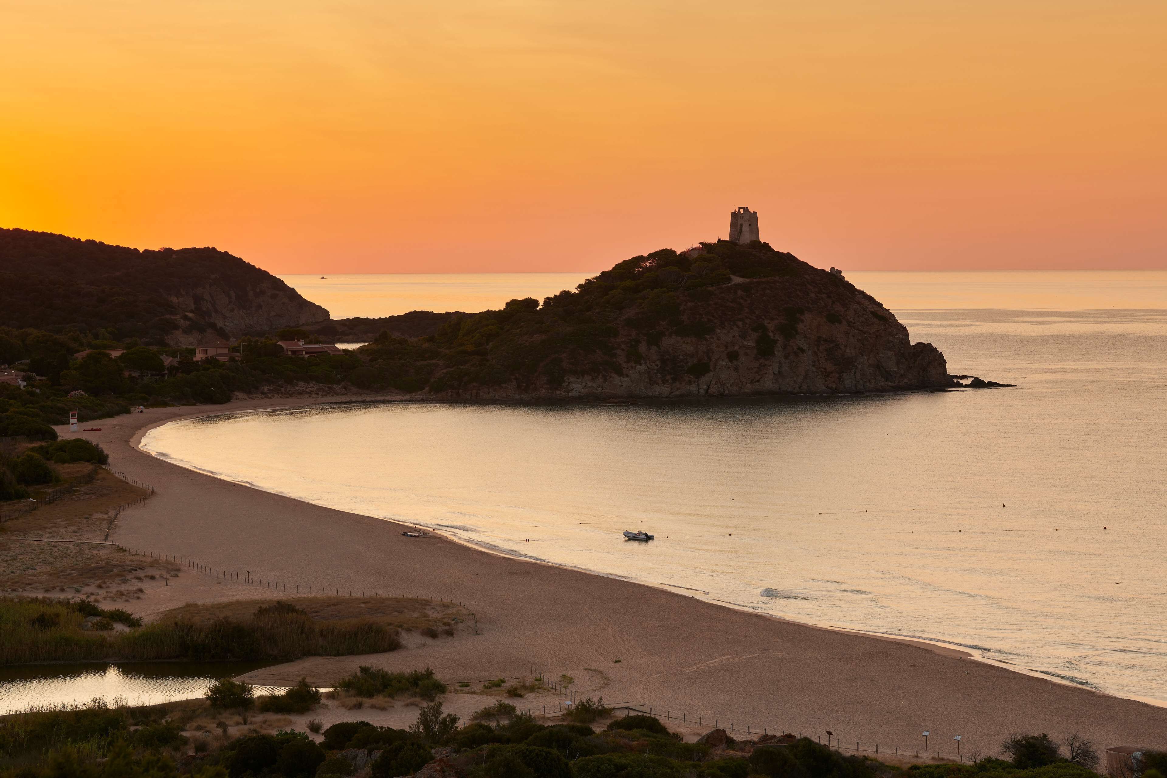 Un paysage côtier avec un château perché sur une colline, une plage en forme de courbe et une mer calme.