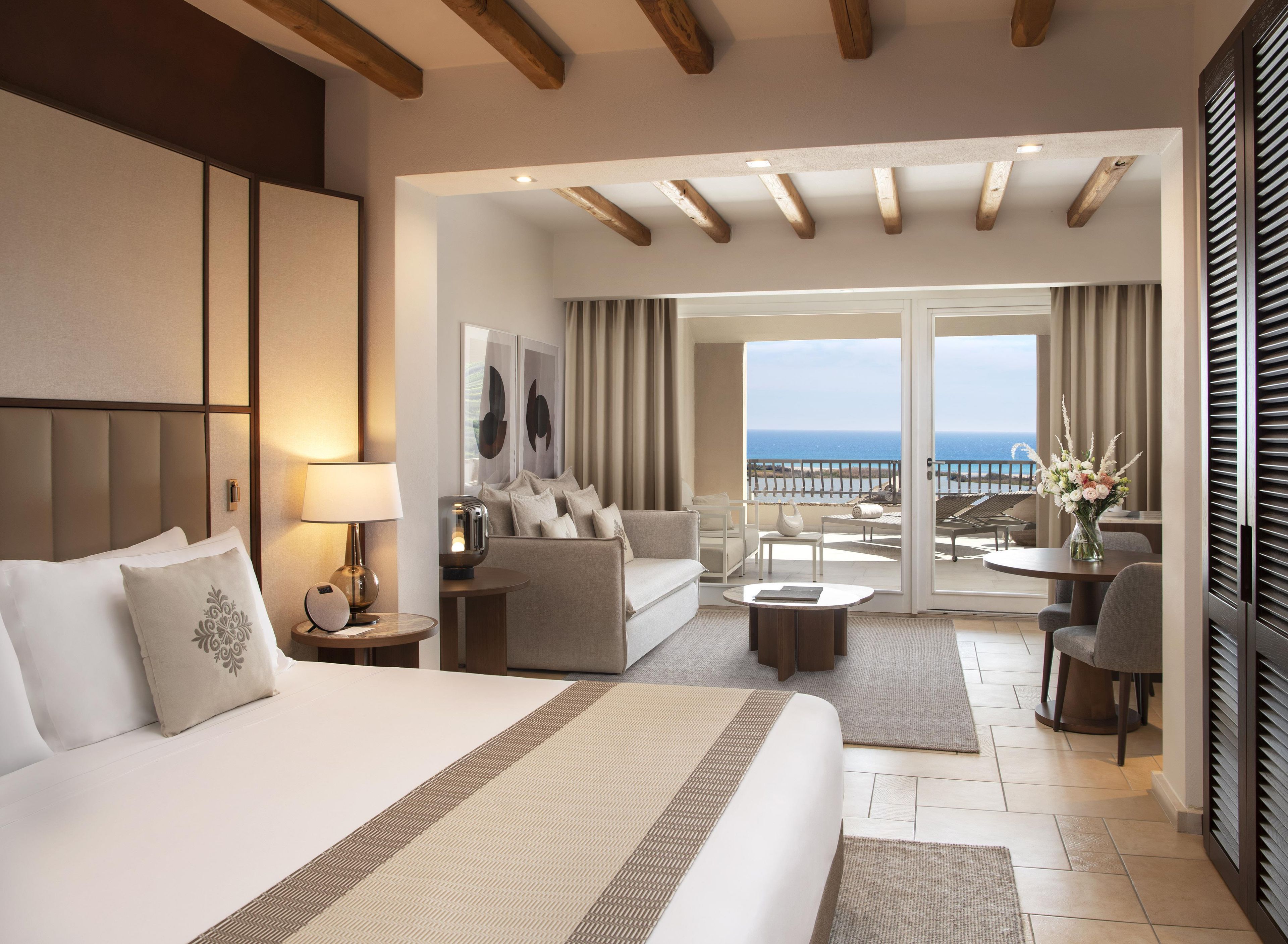 A hotel room with a bed, a sofa, a coffee table, and a balcony with a view of the sea.