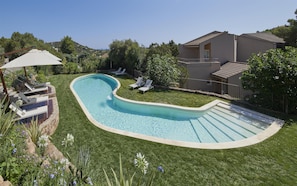 Uma piscina com design curvo, rodeada por um gramado bem cuidado e uma casa com telhado em telhas.
