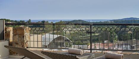 A balcony with a view of a coastal landscape, including a building and greenery.