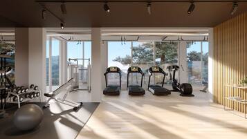 A spacious gym with treadmills, dumbbells, and exercise balls, large windows offering a view of the outdoors.