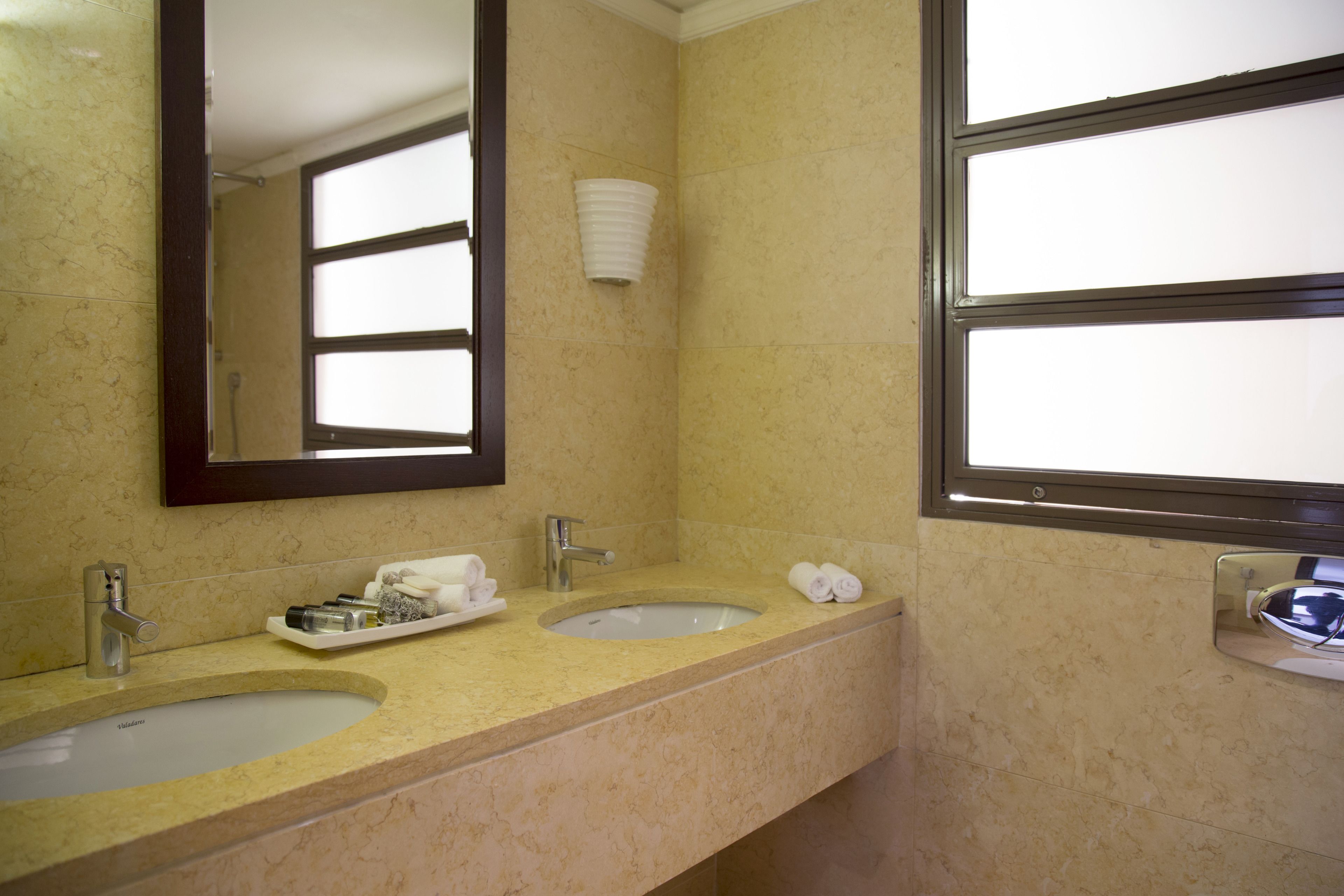 Baño con dos lavamanos, un espejo y una ventana.