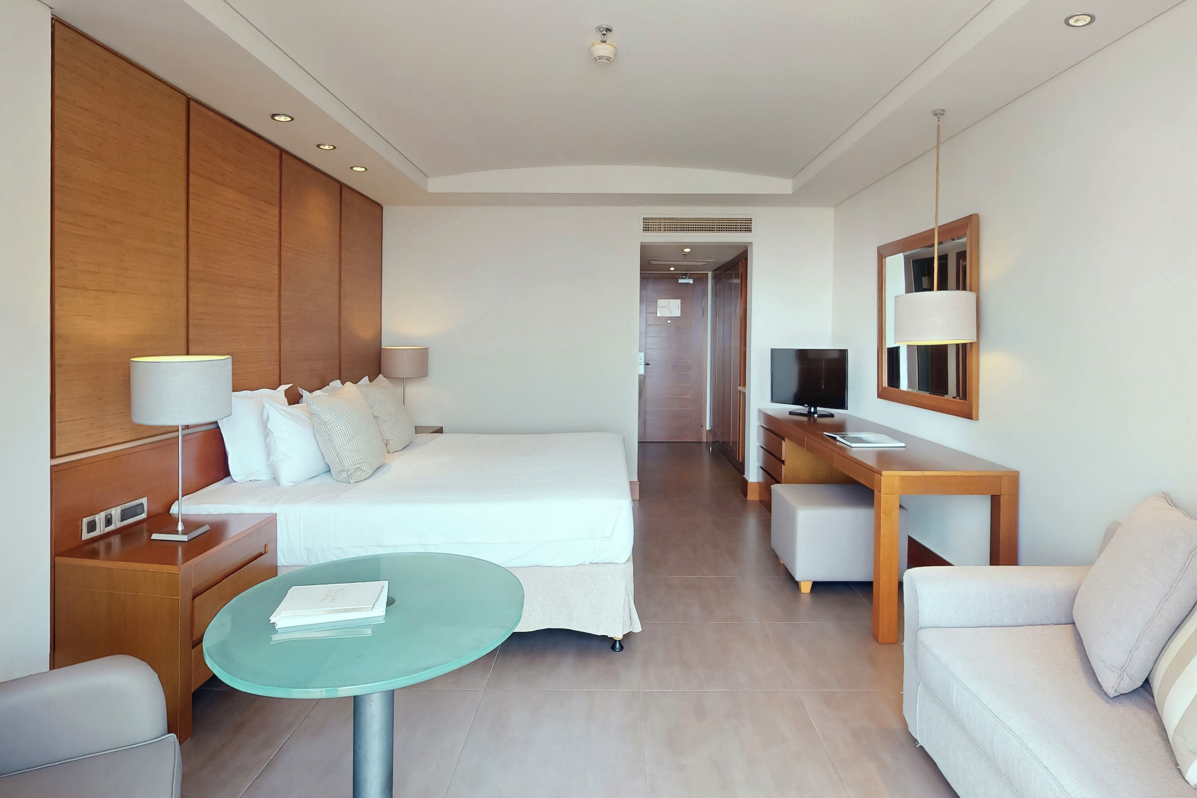 A hotel room with a bed, bedside tables, a desk, a TV, and a seating area.