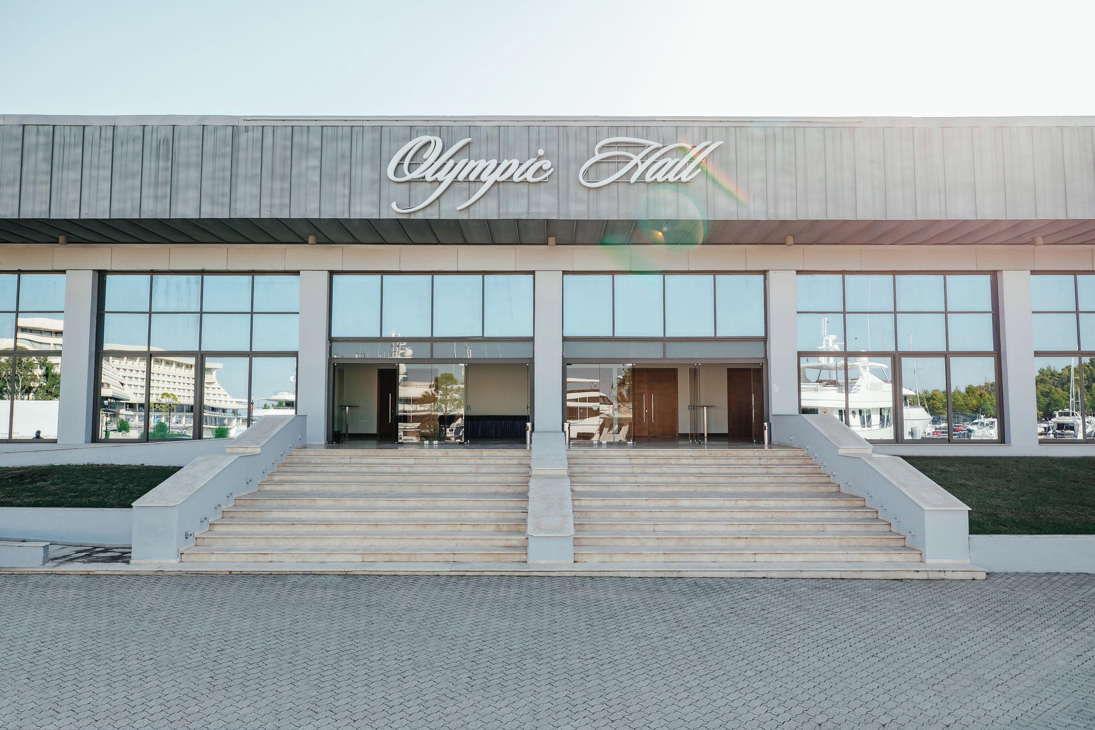 The exterior of the Olympic Hall building with large windows and a set of stairs leading to the entrance.