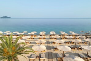 A beach with rows of sun loungers and thatched umbrellas, a clear sky, and calm sea. - Porto Carras Meliton (Sithonia)
