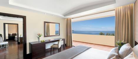 A hotel room with a large bed, a desk, and a view of the sea.