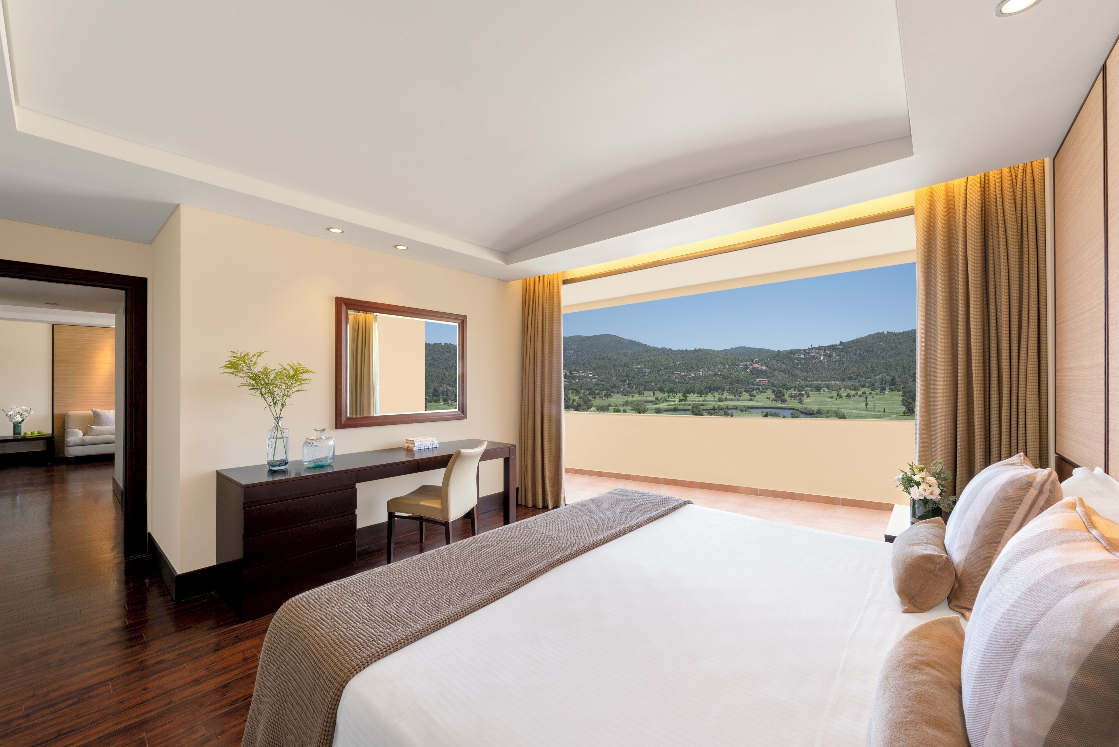A hotel room with a large bed, a desk with a chair, a mirror, and a view of the outdoors.