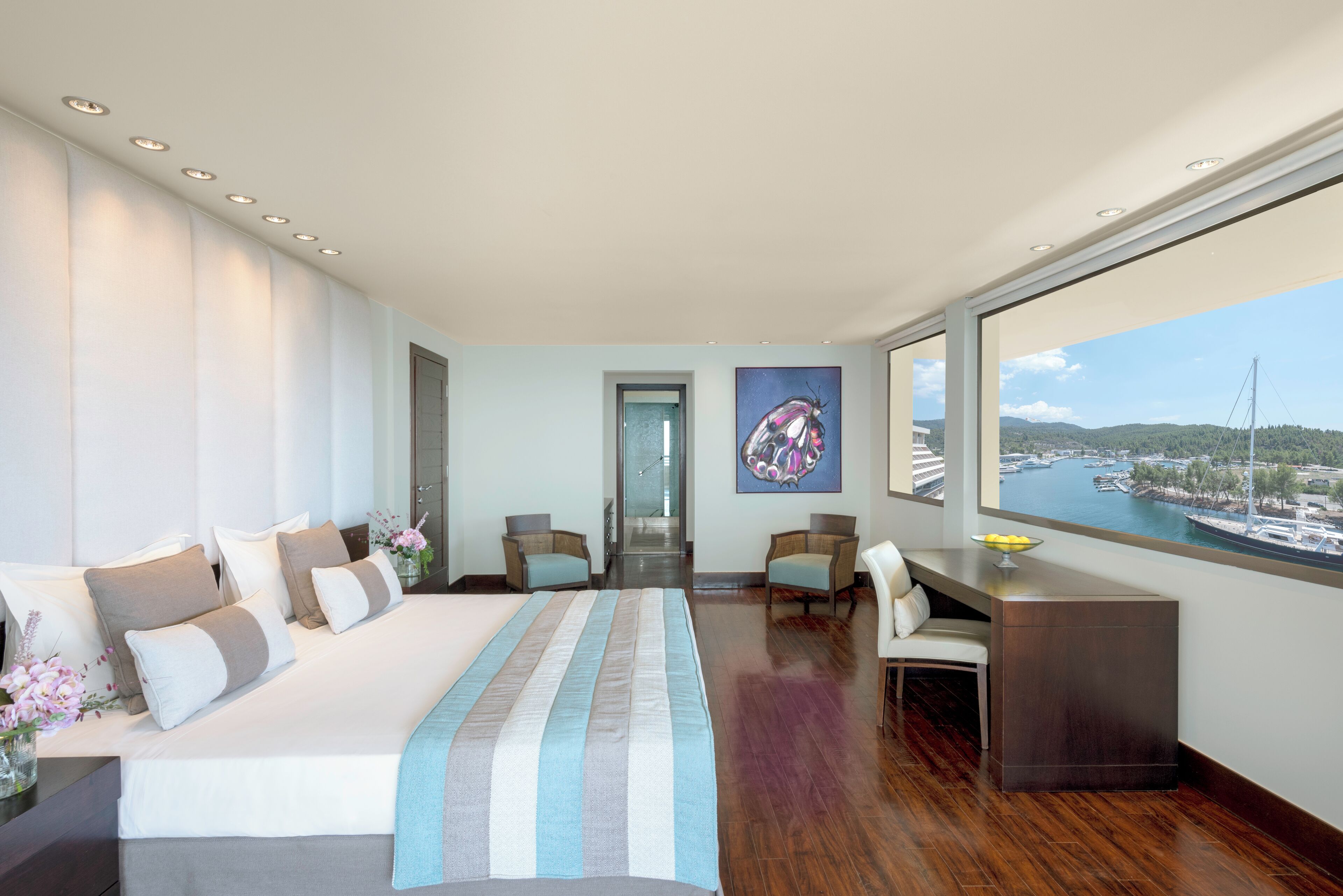 A modern hotel room with a large bed, a desk, and a view of a marina.