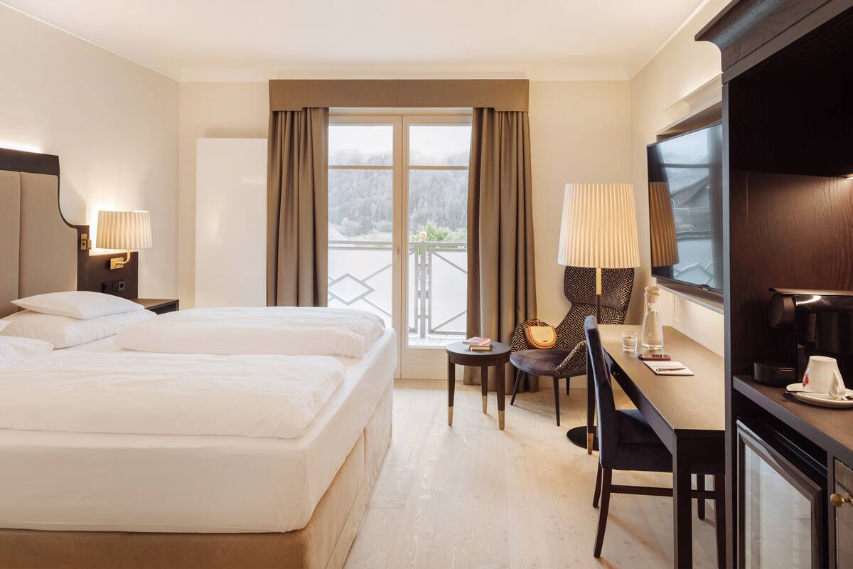 Habitació d'hotel amb llit, escriptori, cadira, televisió i finestra amb cortines.