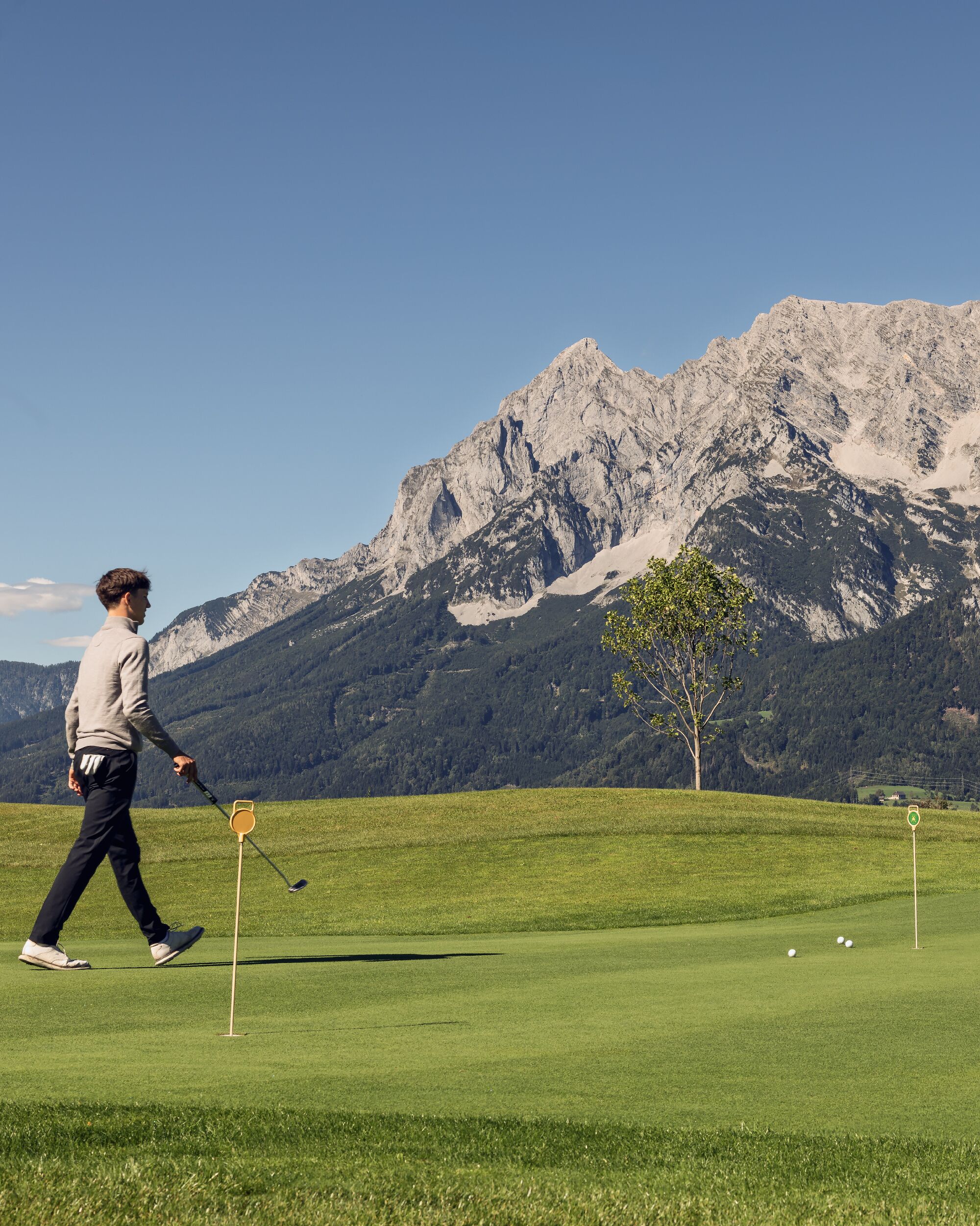 A person walking on a golf course with a mountainous backdrop.