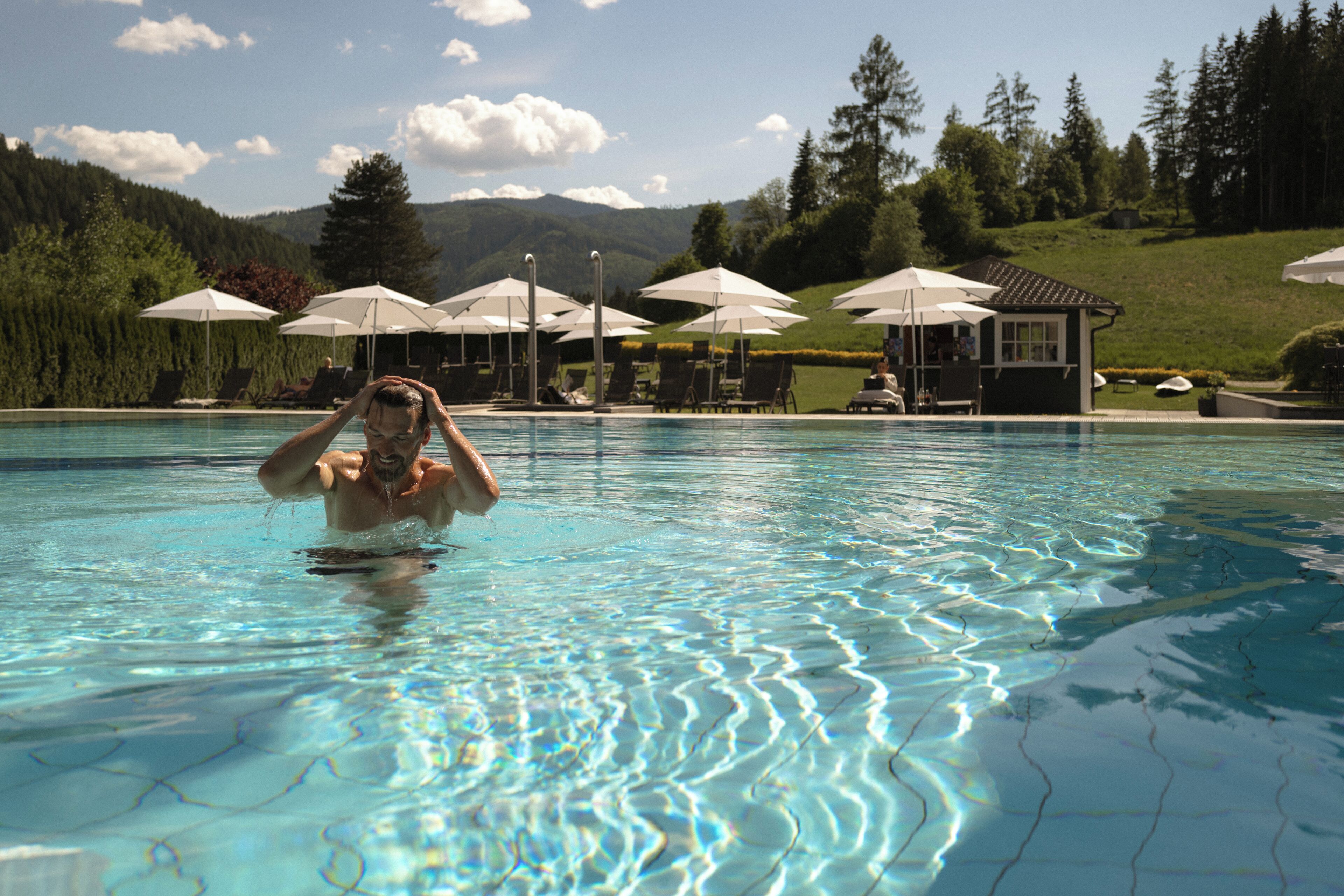 A swimming pool with clear water, lounge chairs, umbrellas, and a view of a hilly landscape.