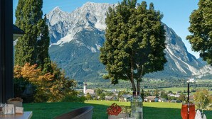A dining area with a table set for two, a view of a mountain, and a tree in the foreground.