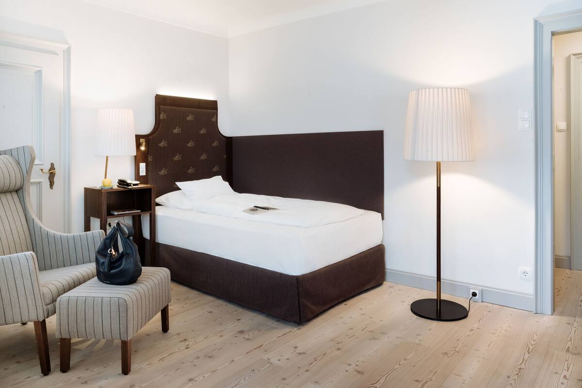 Habitació d'hotel ben ordenada amb un llit, una cadira, una taula de nit, una làmpada i una làmpada de peu.