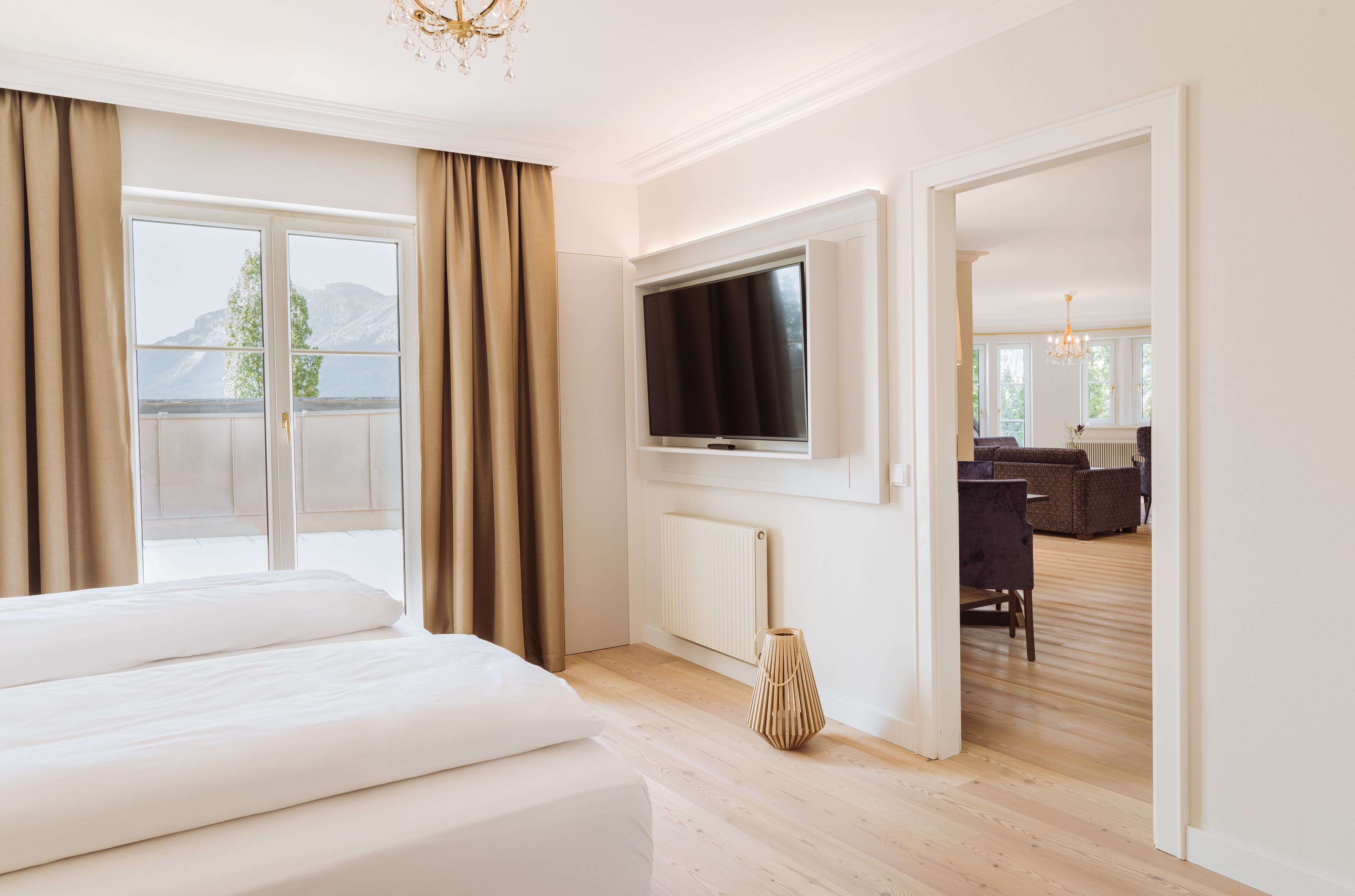 A hotel room with a large bed, a TV mounted on the wall, a radiator, and a view of the outdoors.