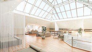 A spacious interior with a high ceiling and a glass roof, featuring a seating area with sofas and a coffee table, and a staircase leading to an upper level.