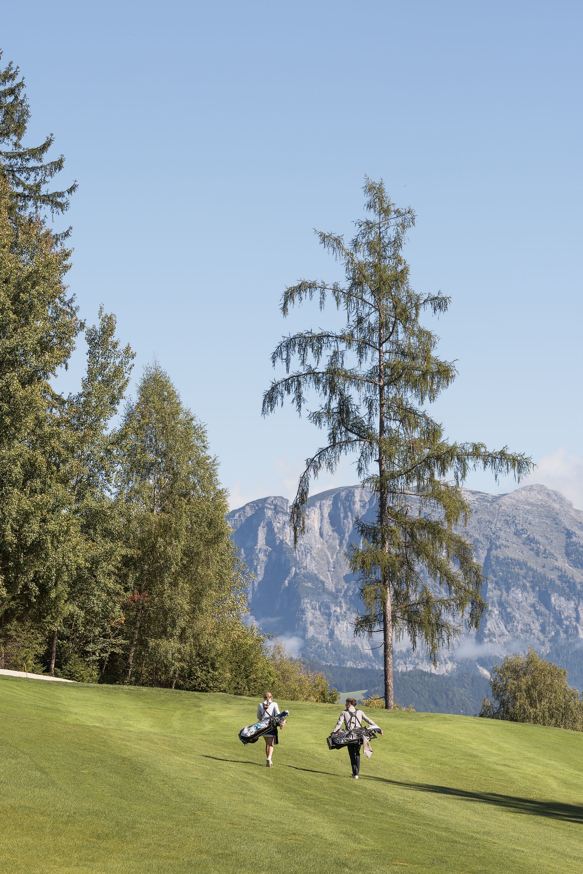 A golf course with a mountainous backdrop, trees, and a clear sky.