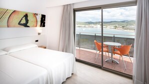 A hotel room with a large bed, a balcony with orange chairs, and a view of the sea and hills. - Hotel THB Ocean Beach - Adults Only (Sant Antoni de Portmany)