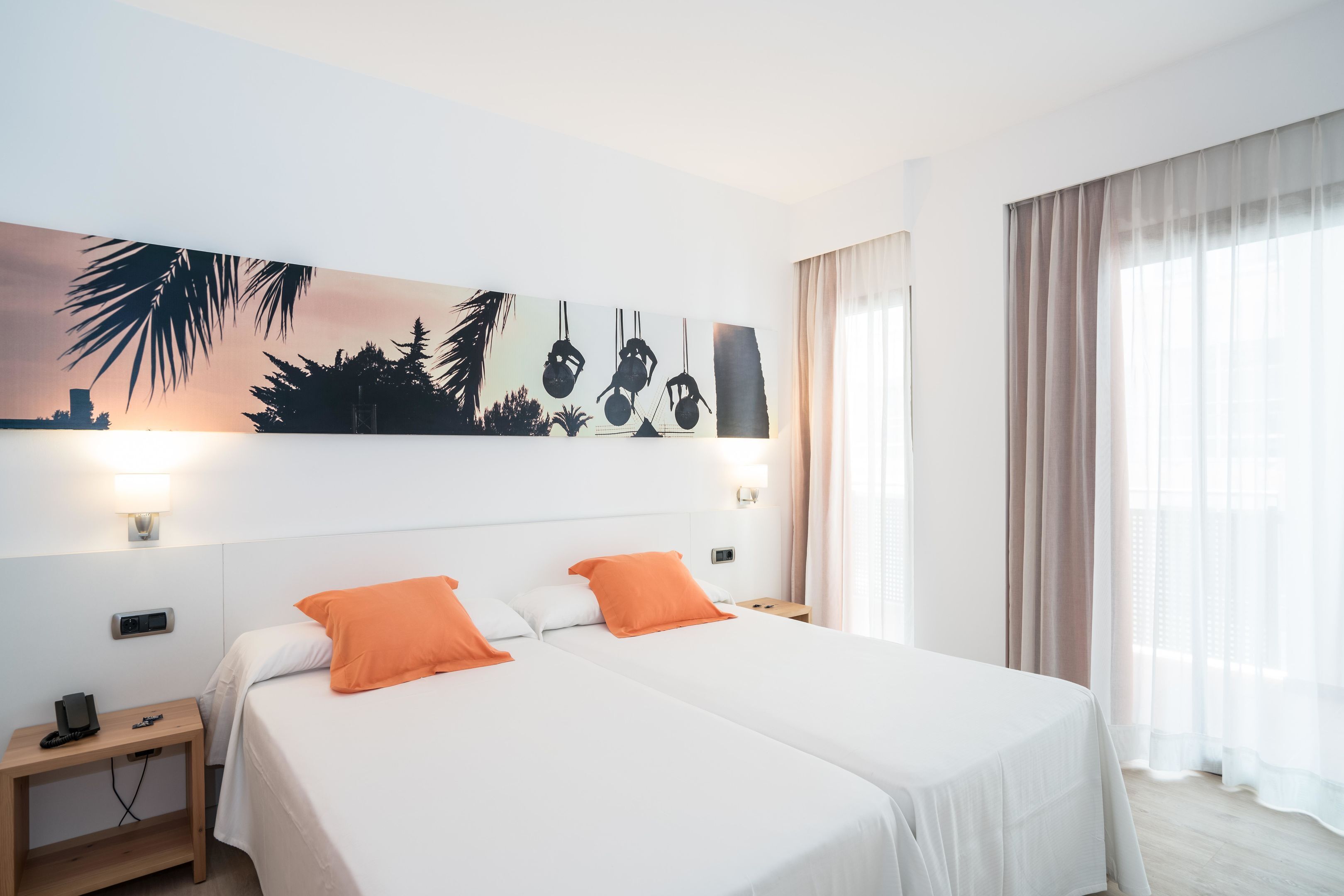 Una habitación de hotel con dos camas, una mesita de noche, un cuadro en la pared y una ventana con cortinas.