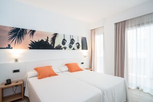 Una habitación de hotel con dos camas, una mesita de noche, un cuadro en la pared y una ventana con cortinas.