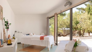 A spa room with a massage table, a small desk with a mirror, and a window with a view of trees. - Hotel THB Ocean Beach - Adults Only (Sant Antoni de Portmany)
