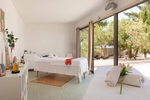 A spa room with a massage table, a small desk with a mirror, and a window with a view of trees. - Hotel THB Ocean Beach - Adults Only (Sant Antoni de Portmany)