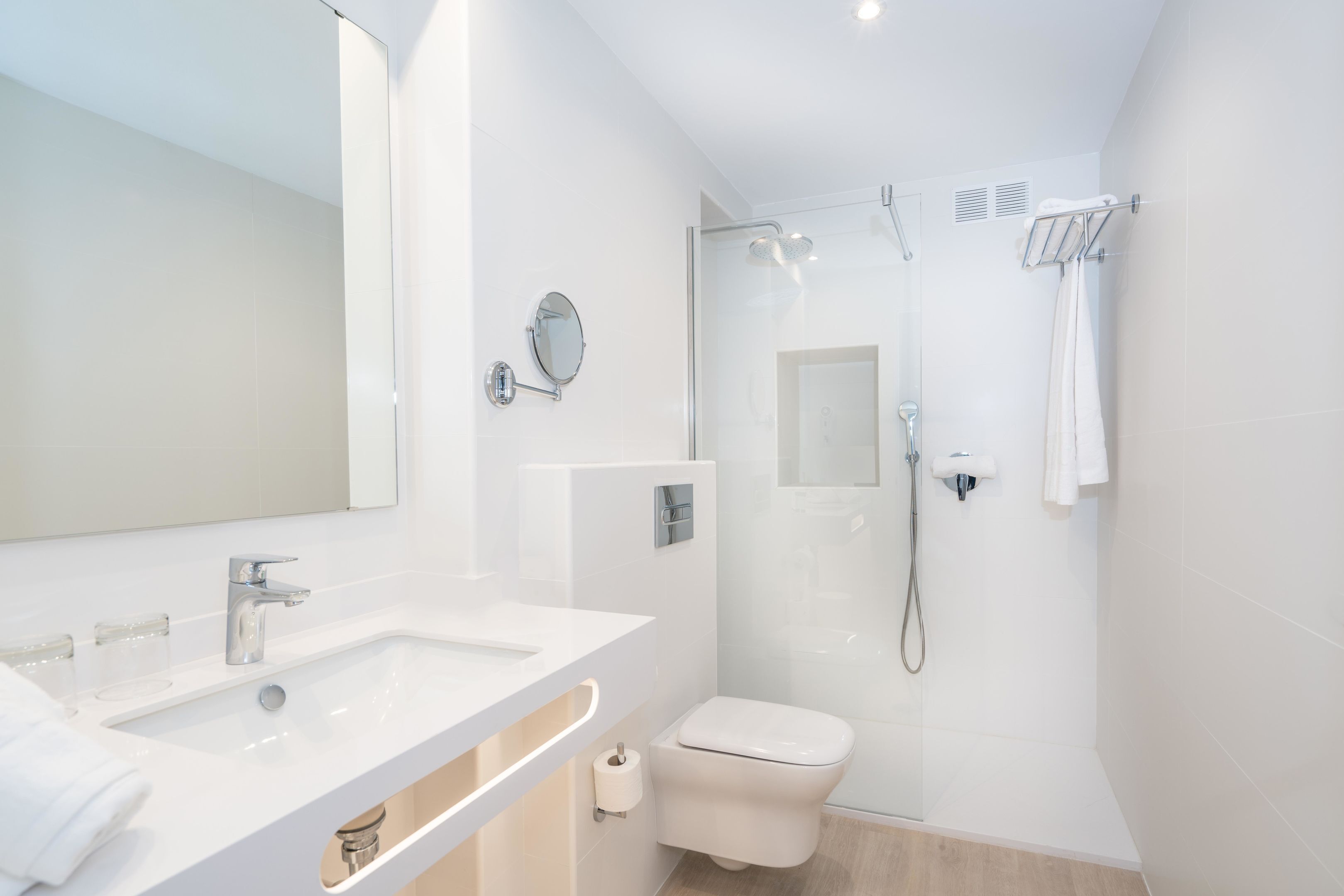 Uma casa de banho moderna com lavatório branco, espelho e sanita, e área de duche separada por vidro.