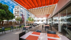An outdoor dining area with tables and chairs, a wooden deck, and a covered section with a red canopy. - Hotel THB Ocean Beach - Adults Only (Sant Antoni de Portmany)