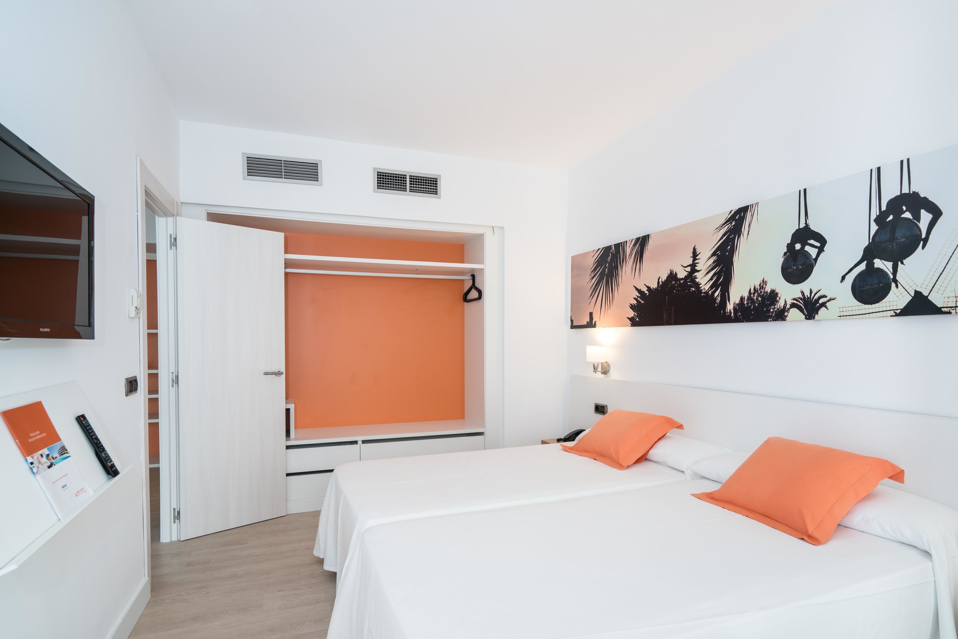 Une chambre d’hôtel avec deux lits, un placard ouvert et un tableau représentant une scène de plage.