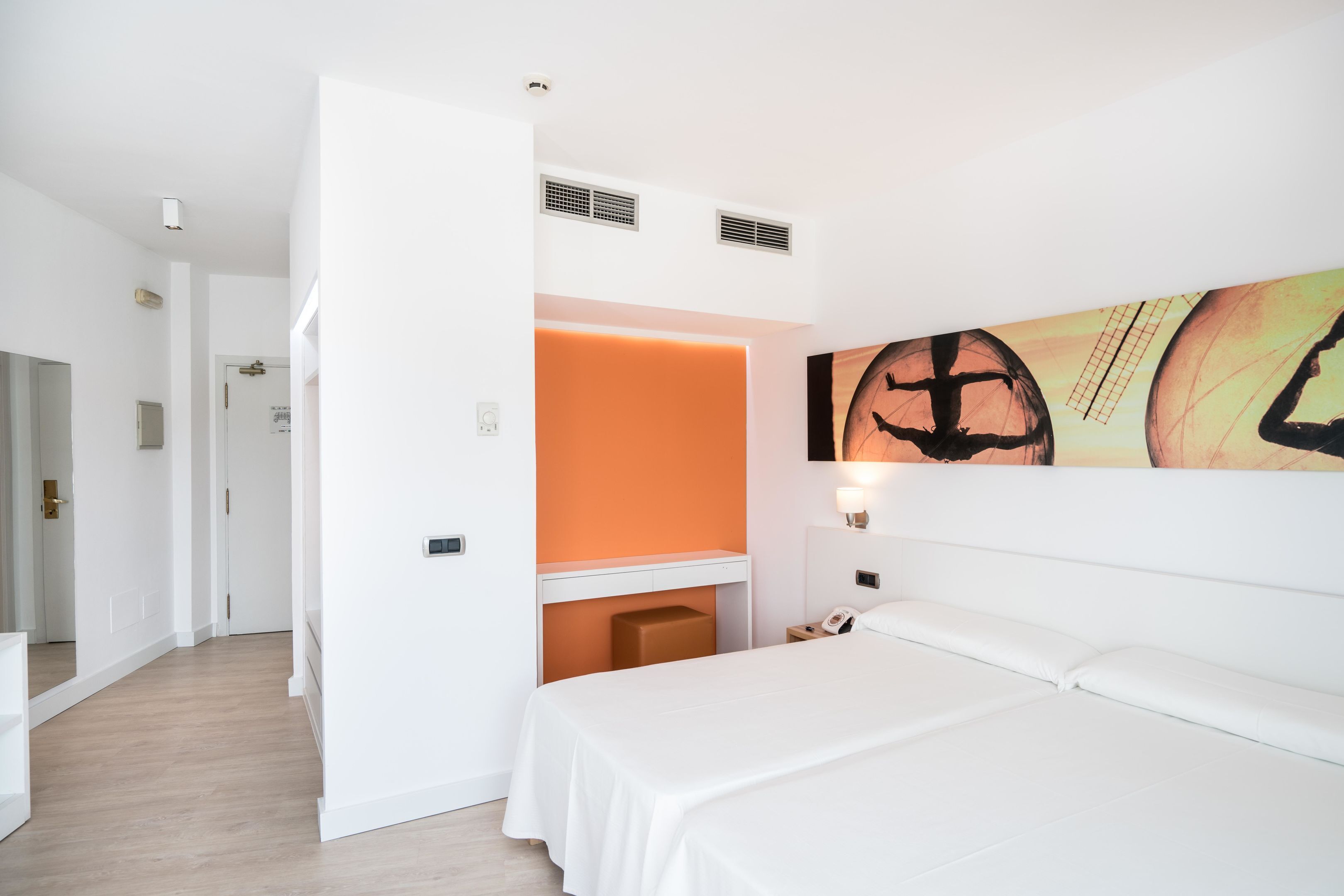 A hotel room with a bed, a desk, and a wall-mounted artwork.