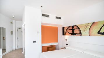 A hotel room with a bed, a desk, and a wall-mounted artwork.