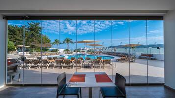 A view from a room with large windows overlooking a pool area with sun loungers and umbrellas.