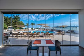 A view from a room with large windows overlooking a pool area with sun loungers and umbrellas.