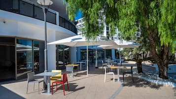 Een terras met tafels en stoelen, omgeven door bomen en een modern gebouw.