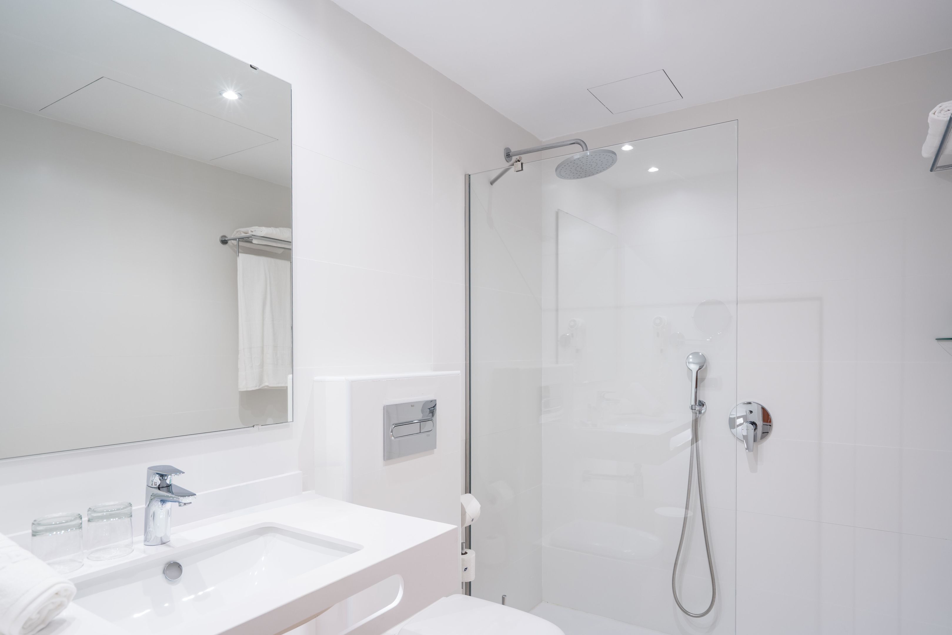 Un baño moderno con lavamanos blanco, espejo y cabina de ducha de vidrio.