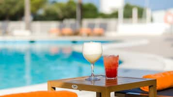 A poolside table with a glass of white drink and a red drink, surrounded by orange cushions.