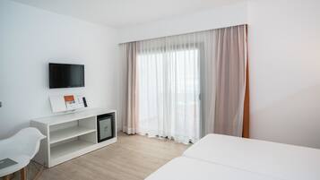 Habitación de hotel con cama, escritorio con computadora, televisor montado en la pared y ventana con cortinas traslúcidas.