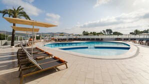 A swimming pool area with sun loungers and umbrellas, surrounded by a tiled deck and palm trees. - Hotel THB Ocean Beach - Adults Only (Sant Antoni de Portmany)