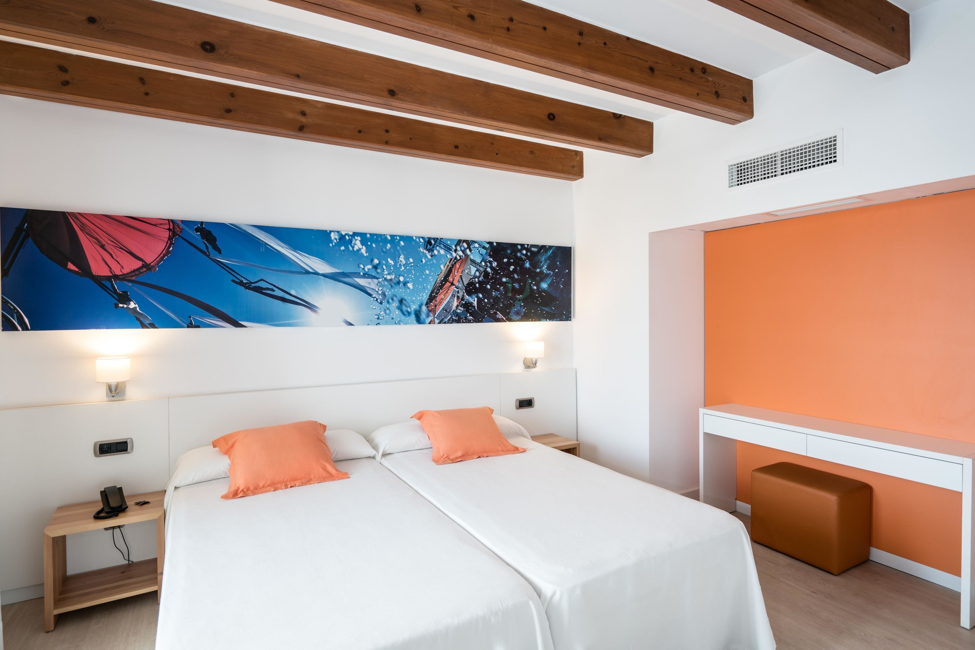 Una habitación de hotel moderna con una cama grande, dos mesitas de noche, un escritorio y un cuadro abstracto de gran tamaño en la pared.