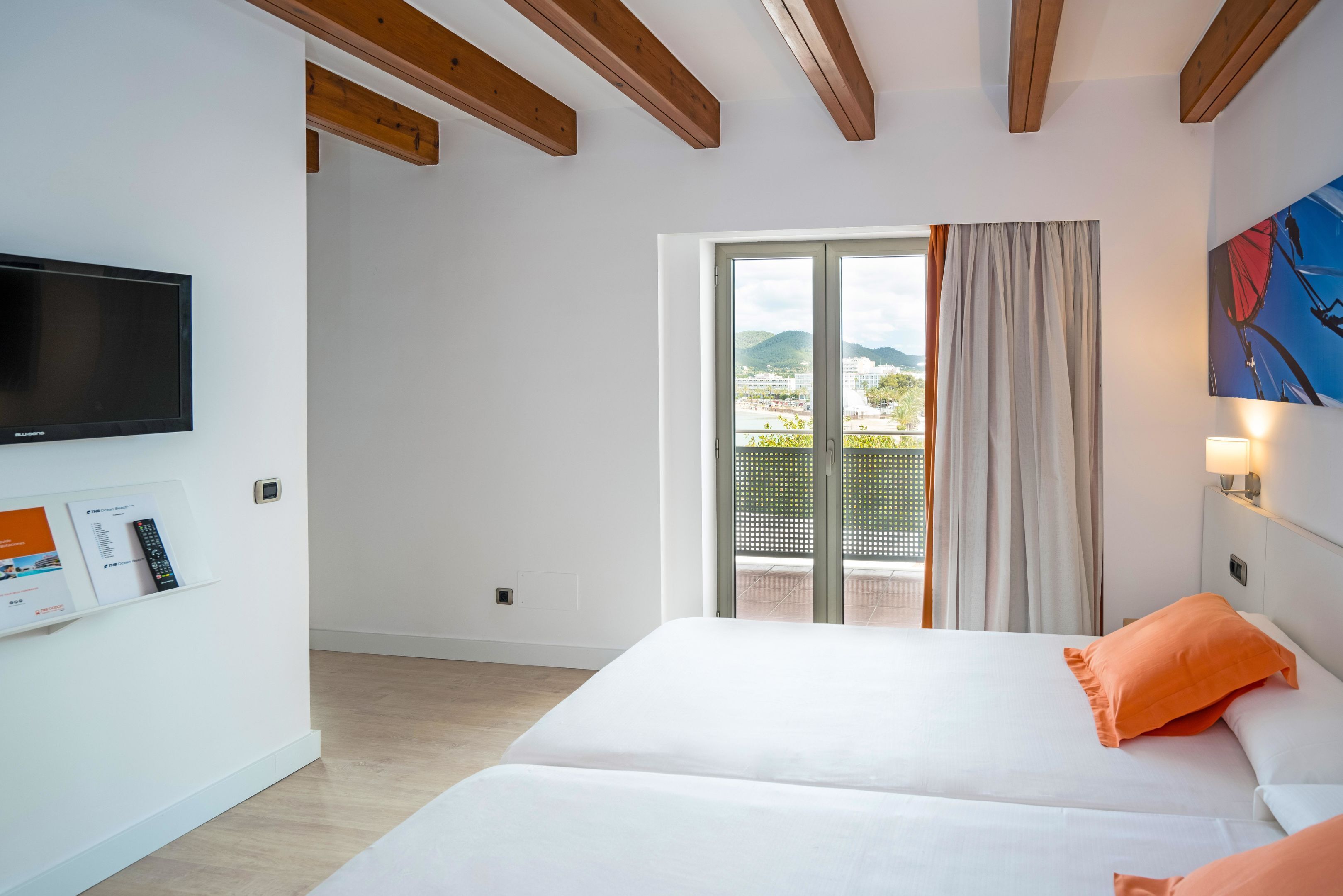A hotel room with a bed, a TV, a window with curtains, and a view of the outside.