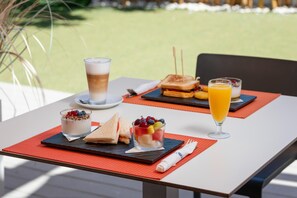 Una colazione con un panino, una ciotola di frutta e un bicchiere di succo d'arancia su un tavolo.