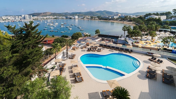 A resort with a large swimming pool, sun loungers, and a view of the marina. - Hotel THB Ocean Beach - Adults Only (Sant Antoni de Portmany)