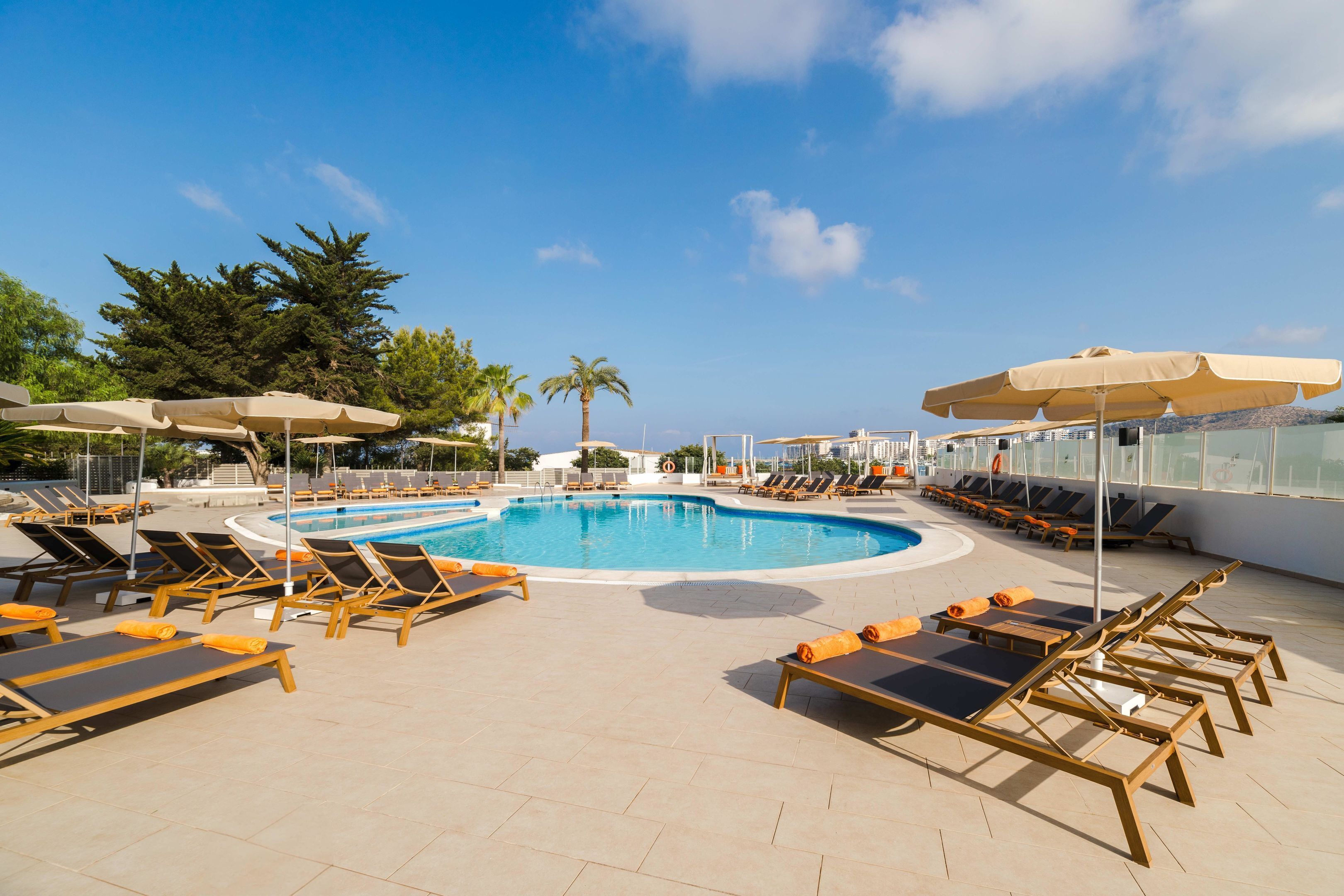 A poolside area with sun loungers, umbrellas, and a clear blue sky.