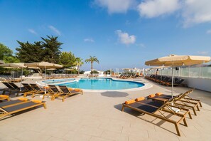 Ein Poolbereich mit Liegestühlen, Sonnenschirmen und blauem Himmel.
