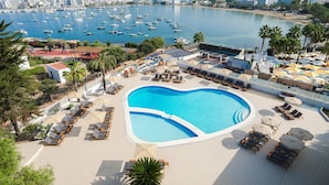 A heart-shaped pool with sun loungers and umbrellas, surrounded by a beachside view with boats and buildings. - Hotel THB Ocean Beach - Adults Only (Sant Antoni de Portmany)