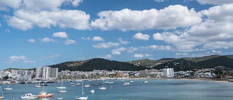 Un pueblo costero con un puerto deportivo lleno de barcos, una playa y colinas al fondo.
