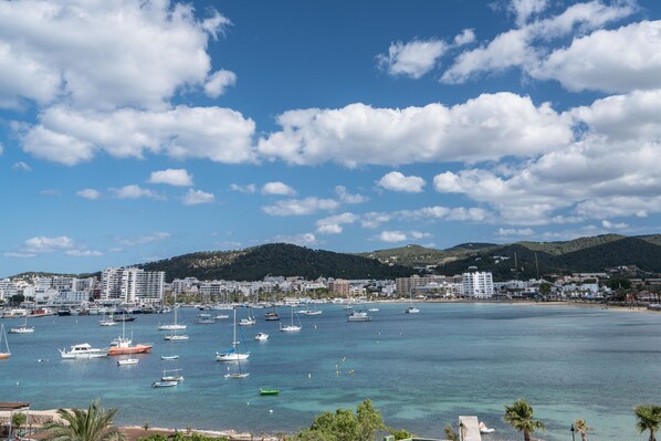 A coastal town with a marina filled with boats, a beach, and a backdrop of hills.